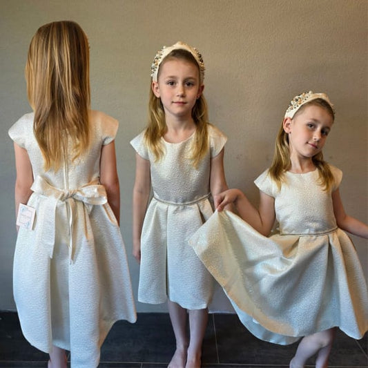 Alt tekst:
Luxe meisjesjurk in ivoor champagnekleur met elegante jacquard-look en hi-low rok uit de Petite Occasion Dresses collectie van Jacobsz Atelier.